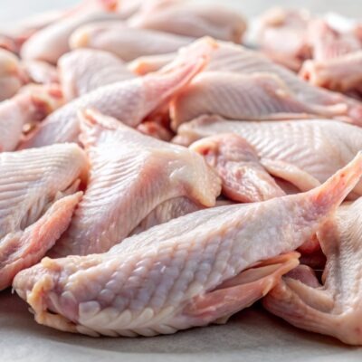 Alitas de pollo crudas recién compradas, con la piel aún intacta, esparcidas sobre una superficie blanca, relucientes por la humedad, a la espera de ser cocinadas o sazonadas para una sabrosa comida.
